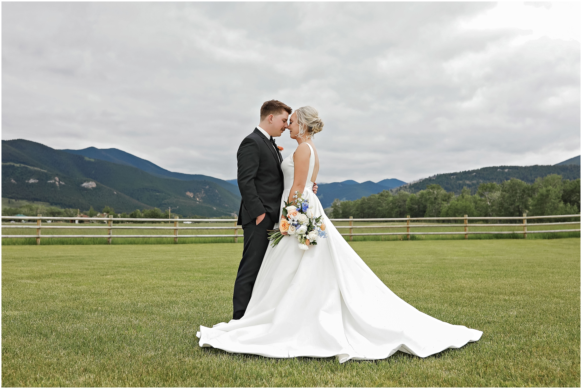Bride and groom standing in green grass in front of mountains at Venue 406 Wedding