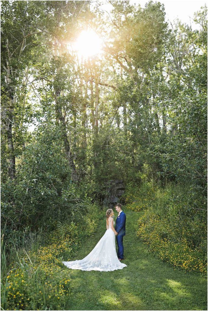 MT Wildflower Wedding Bride and Groom standing near waterfall with sun shining through trees